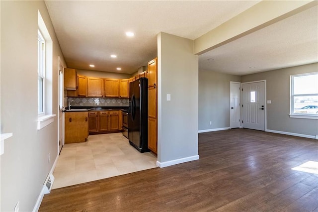 kitchen with light wood-style floors, decorative backsplash, dark countertops, and freestanding refrigerator