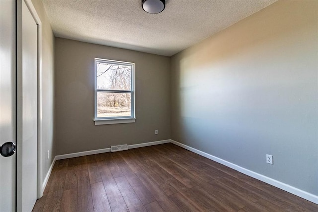 unfurnished room featuring a textured ceiling, dark wood-style floors, visible vents, and baseboards