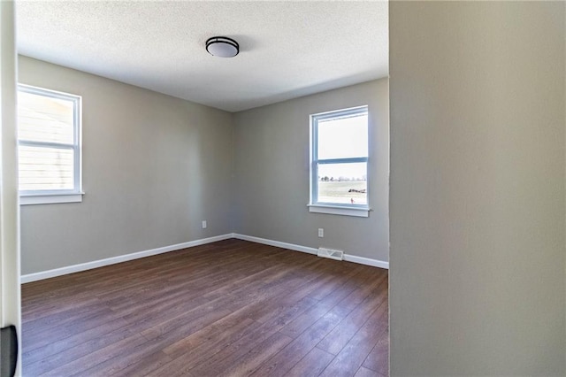 unfurnished room with visible vents, a textured ceiling, dark wood-type flooring, and baseboards