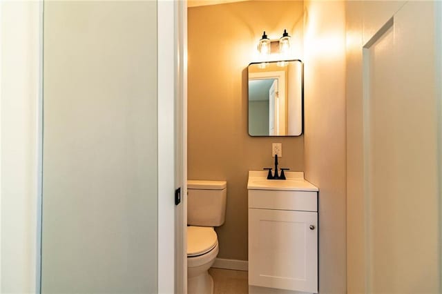 half bathroom with baseboards, toilet, and vanity