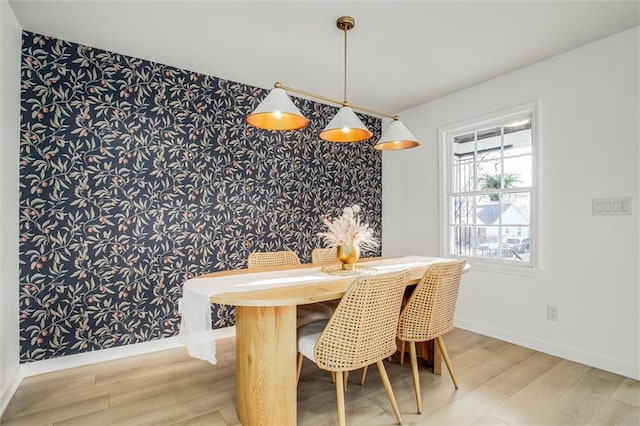 dining room with baseboards, wood finished floors, an accent wall, and wallpapered walls