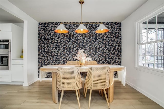 dining area featuring baseboards, light wood-style floors, an accent wall, and wallpapered walls