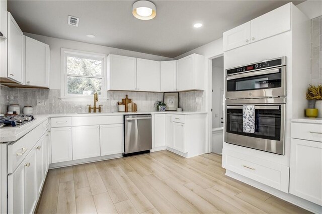 kitchen with a sink, visible vents, backsplash, and stainless steel appliances