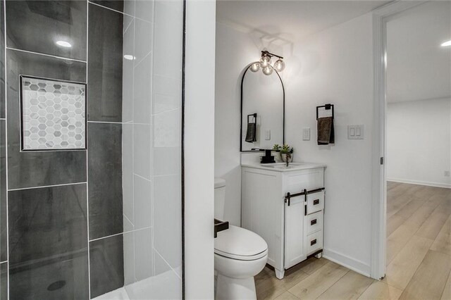 full bath with toilet, wood finished floors, tiled shower, baseboards, and vanity