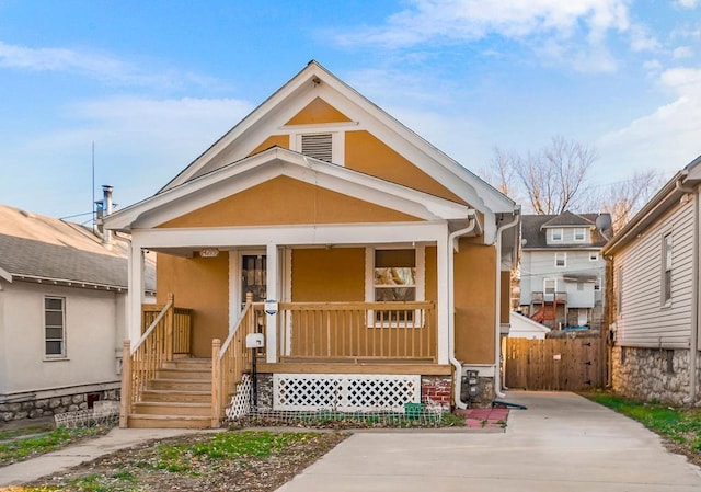 view of front of home with stucco siding, a porch, and fence