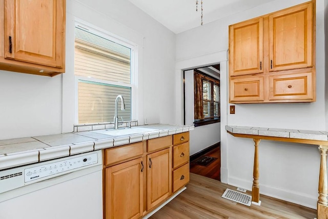 kitchen featuring light wood-type flooring, visible vents, a sink, baseboards, and dishwasher