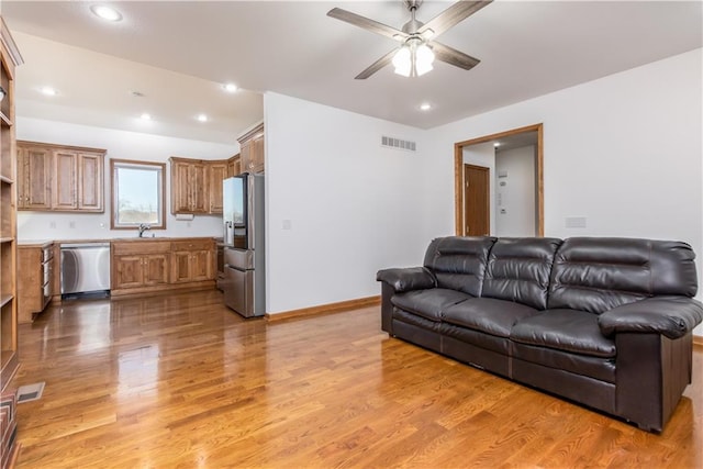 living area with light wood-style flooring, baseboards, visible vents, and ceiling fan