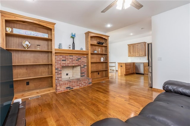 living room featuring visible vents, a fireplace, light wood-style flooring, and a ceiling fan