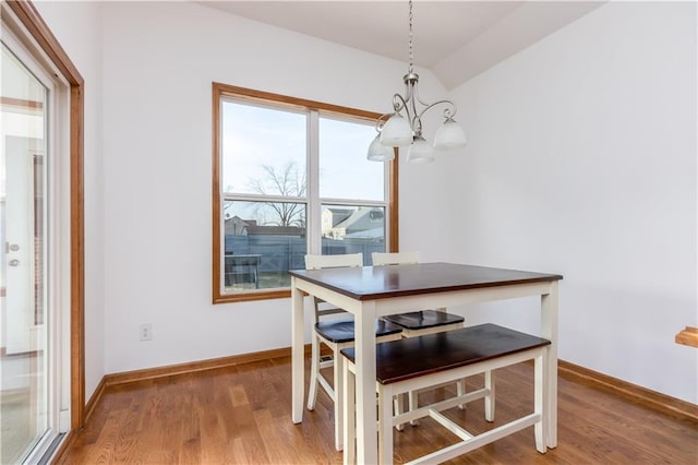 dining area featuring baseboards, an inviting chandelier, vaulted ceiling, and light wood finished floors