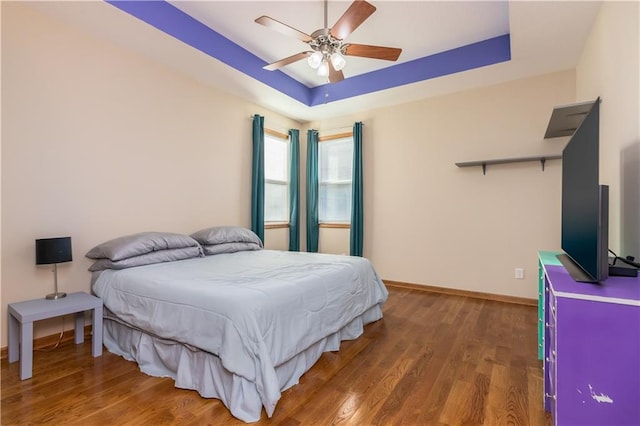 bedroom featuring ceiling fan, baseboards, a tray ceiling, and wood finished floors