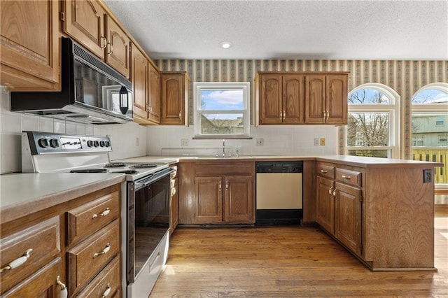 kitchen with wallpapered walls, a peninsula, electric range, white dishwasher, and a sink