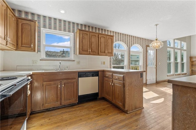 kitchen with white appliances, wallpapered walls, a peninsula, a sink, and a notable chandelier