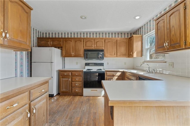 kitchen featuring wallpapered walls, light countertops, wood finished floors, white appliances, and a sink