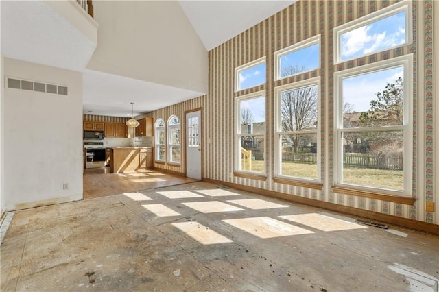 unfurnished living room with wallpapered walls, baseboards, visible vents, and high vaulted ceiling