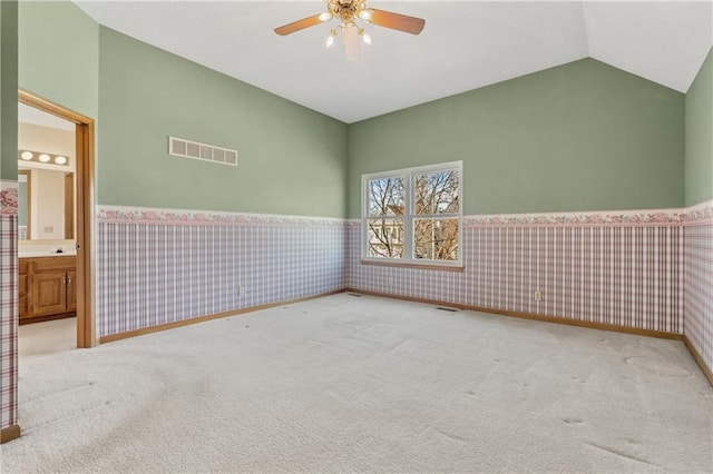 carpeted empty room with visible vents, wallpapered walls, a wainscoted wall, lofted ceiling, and a ceiling fan