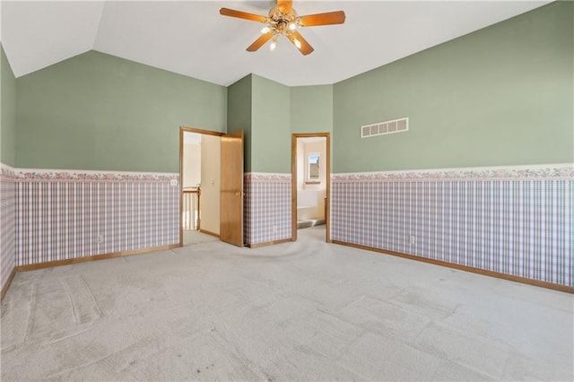 spare room with visible vents, wallpapered walls, ceiling fan, a wainscoted wall, and vaulted ceiling