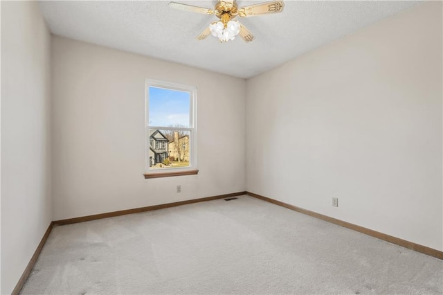 spare room with a ceiling fan, visible vents, baseboards, a textured ceiling, and light carpet