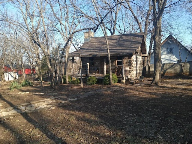 view of front facade featuring fence, roof with shingles, covered porch, a chimney, and log exterior