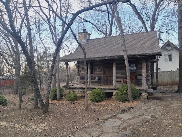 view of front of home featuring log siding, a porch, a chimney, and roof with shingles