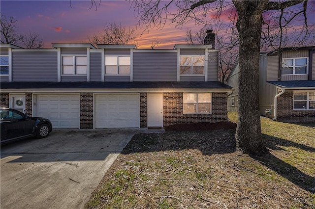 multi unit property featuring a garage, brick siding, a chimney, and driveway