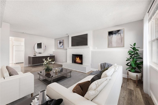 living area with baseboards, a textured ceiling, a brick fireplace, and wood finished floors