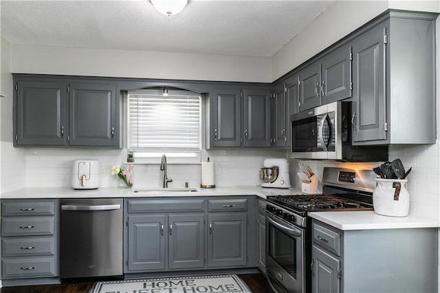 kitchen featuring backsplash, appliances with stainless steel finishes, a sink, gray cabinetry, and light countertops