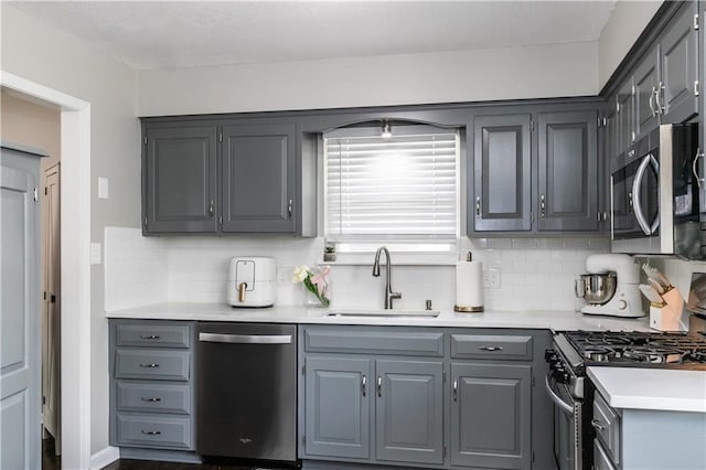 kitchen featuring a sink, light countertops, gray cabinets, stainless steel appliances, and tasteful backsplash