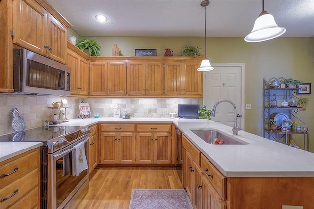 kitchen with a sink, backsplash, light wood-style floors, appliances with stainless steel finishes, and light countertops