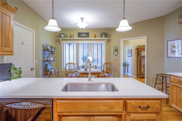 kitchen featuring light wood finished floors, pendant lighting, light countertops, a textured ceiling, and a sink