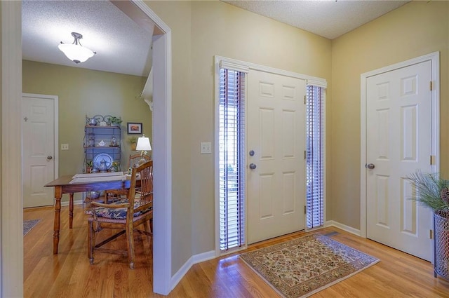 foyer entrance featuring a textured ceiling, baseboards, and wood finished floors