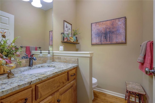 half bathroom featuring vanity, toilet, wood finished floors, and baseboards