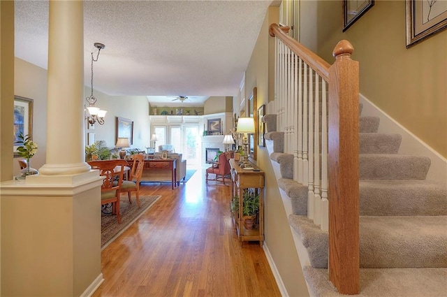 staircase with baseboards, a textured ceiling, wood finished floors, and ornate columns