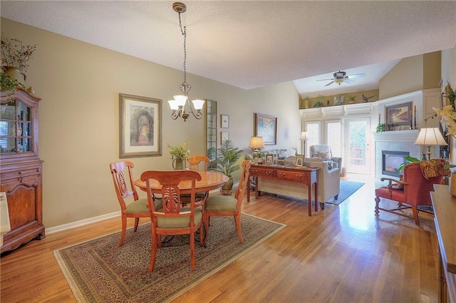 dining space with light wood finished floors, baseboards, vaulted ceiling, a glass covered fireplace, and a textured ceiling