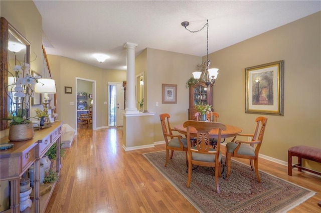 dining space with a notable chandelier, light wood-style floors, baseboards, and ornate columns