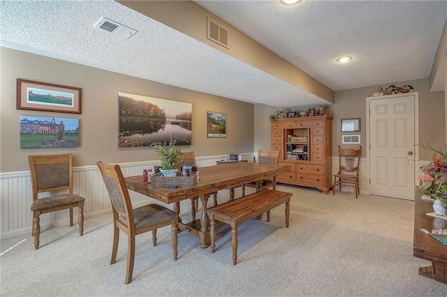 dining area with a wainscoted wall, light colored carpet, visible vents, and a textured ceiling