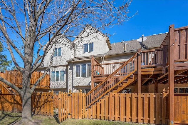 rear view of house featuring a shingled roof, a wooden deck, stairs, and fence