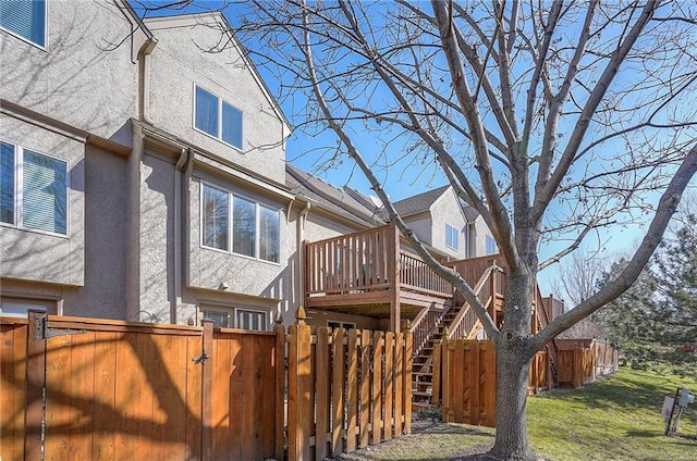 view of home's exterior with stucco siding, a wooden deck, stairs, and fence