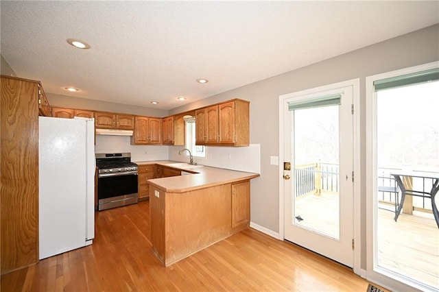 kitchen featuring under cabinet range hood, gas range, a peninsula, freestanding refrigerator, and a sink