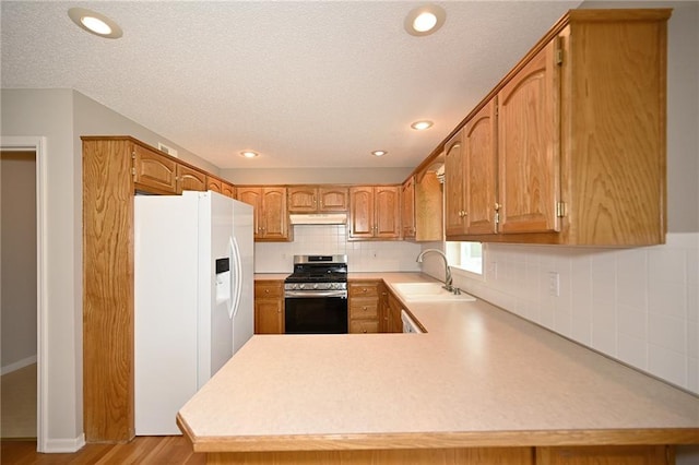 kitchen featuring a sink, light countertops, under cabinet range hood, white fridge with ice dispenser, and stainless steel gas stove