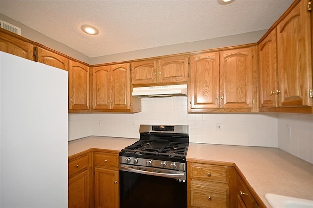 kitchen with stainless steel gas stove, under cabinet range hood, backsplash, freestanding refrigerator, and light countertops