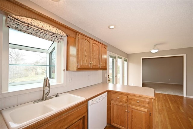 kitchen with a peninsula, white dishwasher, a sink, light countertops, and backsplash