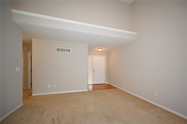 spare room featuring a textured ceiling, carpet, visible vents, and baseboards