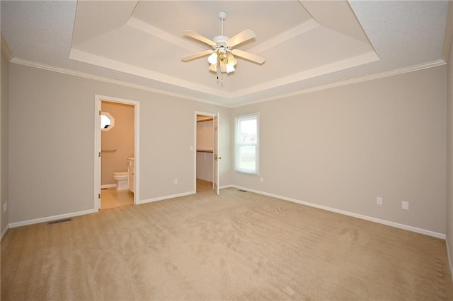 unfurnished bedroom featuring a raised ceiling, ornamental molding, connected bathroom, baseboards, and light colored carpet