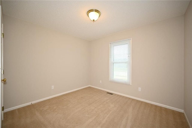 spare room with visible vents, light carpet, a textured ceiling, and baseboards