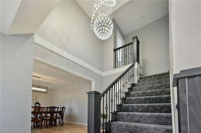 staircase featuring wood finished floors, visible vents, baseboards, a towering ceiling, and a notable chandelier