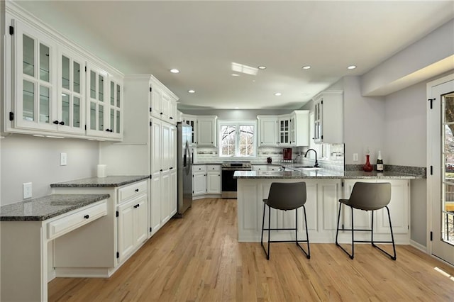 kitchen with glass insert cabinets, light wood-type flooring, appliances with stainless steel finishes, a peninsula, and a sink