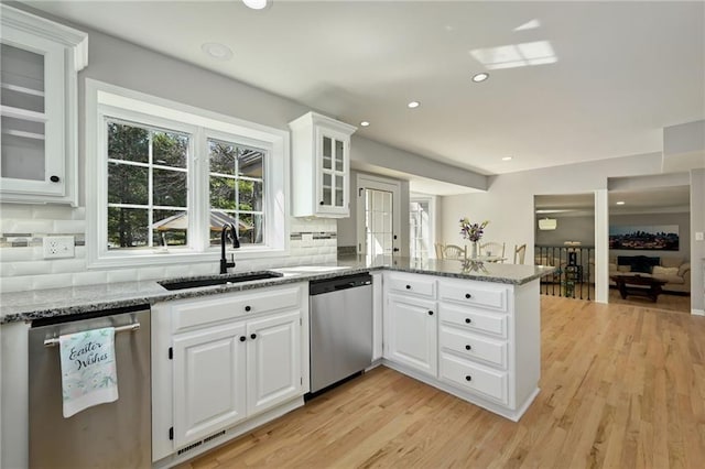 kitchen featuring light wood finished floors, a sink, a peninsula, and stainless steel dishwasher