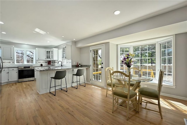 kitchen with electric range, a kitchen breakfast bar, backsplash, white cabinetry, and a peninsula