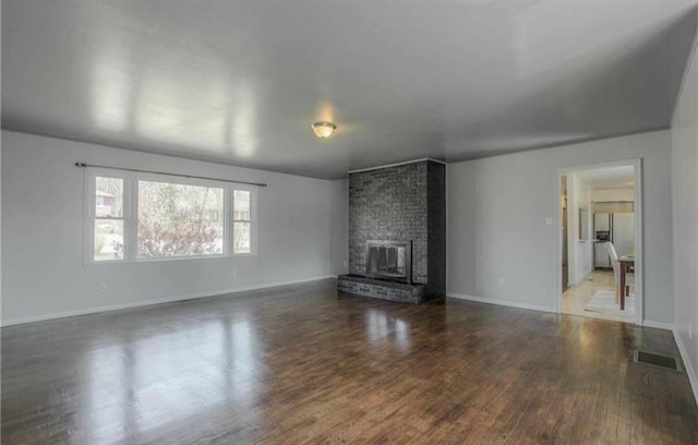 unfurnished living room featuring visible vents, baseboards, a brick fireplace, and wood finished floors