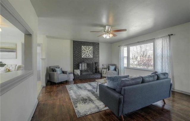 living area with dark wood-type flooring, a brick fireplace, and a ceiling fan